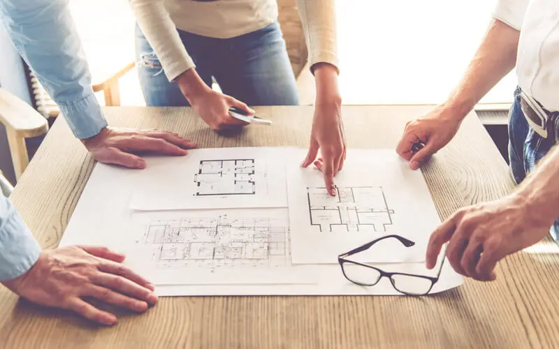 Three people looking at floor plans on a desk